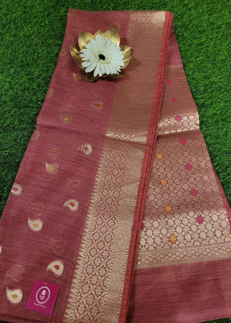 Pink saree with gold patterns and a white flower decoration on a green grass background